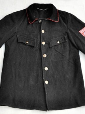 Wollstoff, schwarz, am Kragen und Ärmeln mit roten Paspeln abgesetzt. Knöpfe Messing, große Knöpfe mit Feuerwehremblem (Helm mit gekreuzten Feuerwehräxten), vor 1945, wahrscheinlich um 1930. Sowohl als Einsatzjacke als auch als Uniformjacke getragen. (Nach 1950 abgelöst als Uniformjacke durch die noch heute gebräuchlichen blauen Uniformjacken, als Einsatzjacke abgelöst durch den -Feuerwehrschutzanzug (1)-)